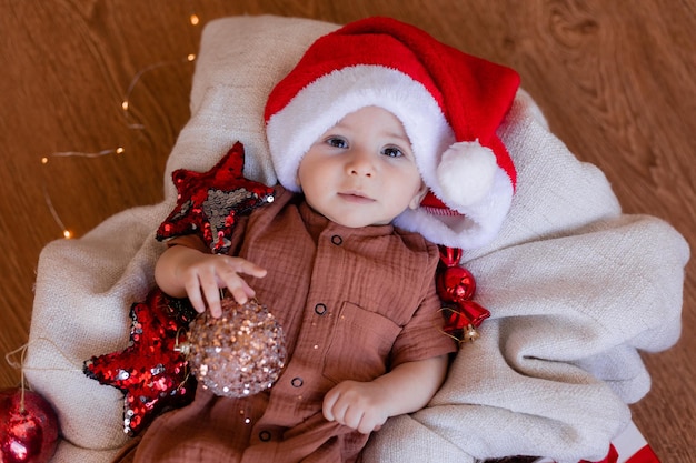 Süßes Baby in einer Weihnachtsmütze liegt in einer Decke auf dem Boden und hält einen Weihnachtsball in der Hand. schöne Ferien. winter, neujahr. Foto in hoher Qualität