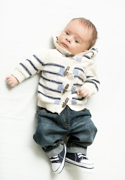 Süßes Baby in Jeans und Pullover auf dem Bett liegend