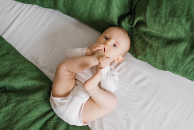 Süßes Baby liegt auf einer grün-weißen Tagesdecke auf dem Bett Ein lächelndes Kind, das seine Füße hat