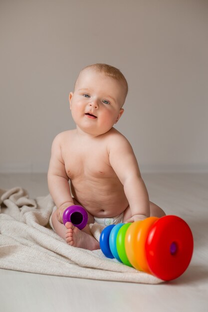 Süßes Baby liegt in Windeln im Bett und sitzt auf dem Boden des Hauses und spielt mit Lernspielzeug