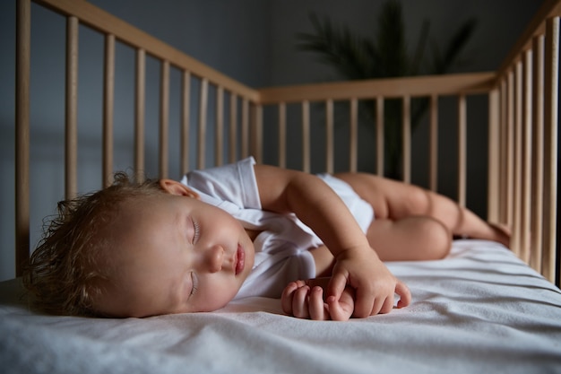 Süßes Baby schläft nachts in einer Wiege für Babys ohne Baldachin und Stoßfänger. sicher schlafen im dunkeln