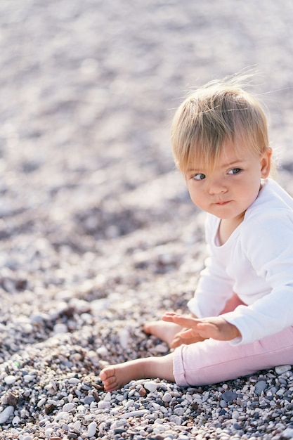 Foto süßes baby sitzt auf einem kiesstrand und schaut weg