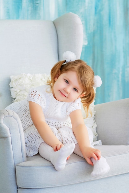 süßes Baby sitzt auf einem Stuhl. glückliches kleines Mädchen mit lockigen blonden Haaren