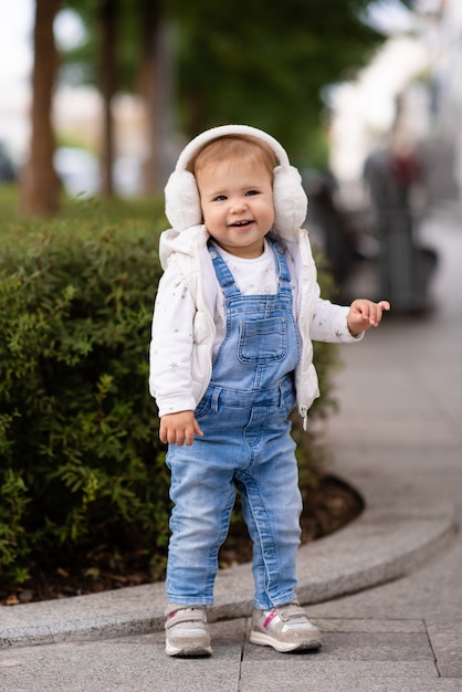 Süßes Baby trägt flauschige weiße Kopfhörer-Denim-Anzughosen und Strickpullover