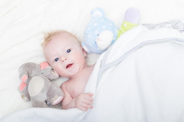 Süßes blondes kleines Baby mit blauen Augen mit seinem Lieblingsplüsch-Teddybär und -Elefanten.