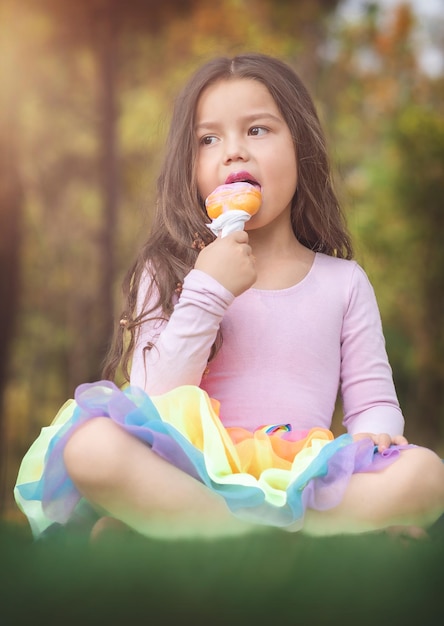 Süßes blondes, lockiges Mädchen, das im Park ein schönes Eis isst, Konzept des Kindertages