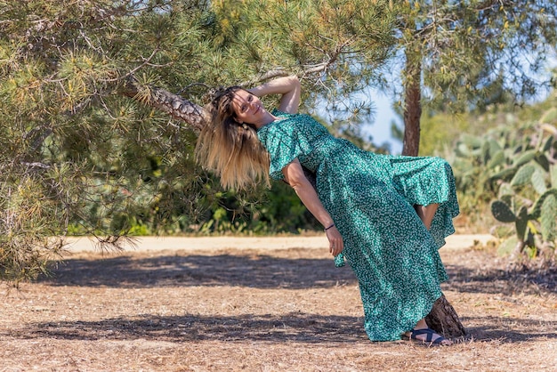 Süßes blondes Mädchen mit grünem Kleid lehnt an einem Baum in einem Park