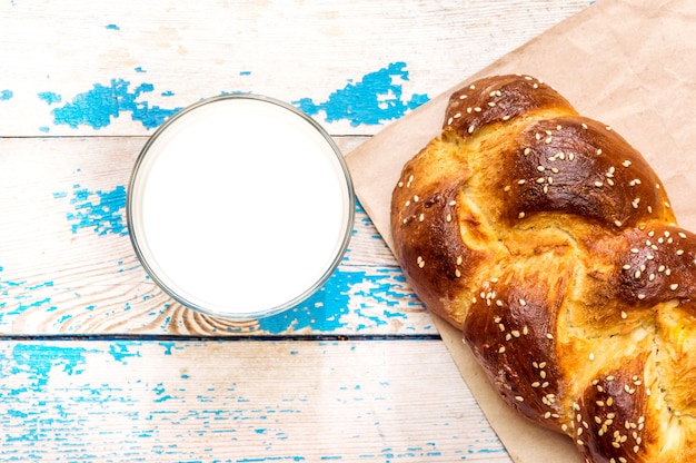 Süßes Brötchen mit Glas Milch auf blauem Holzhintergrund.