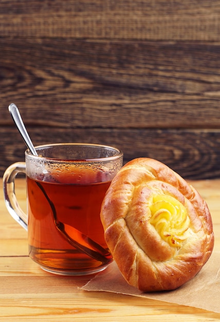 Süßes Brötchen und heiße Tasse Tee auf Holztisch