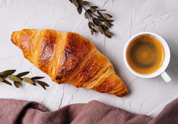 Süßes Croissant mit einer Tasse Kaffee und einem Leinentuch