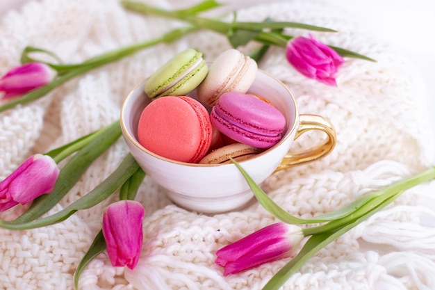 Süßes Dessert, Makronen im goldenen Becher und rosa Tulpen auf Wollhintergrund