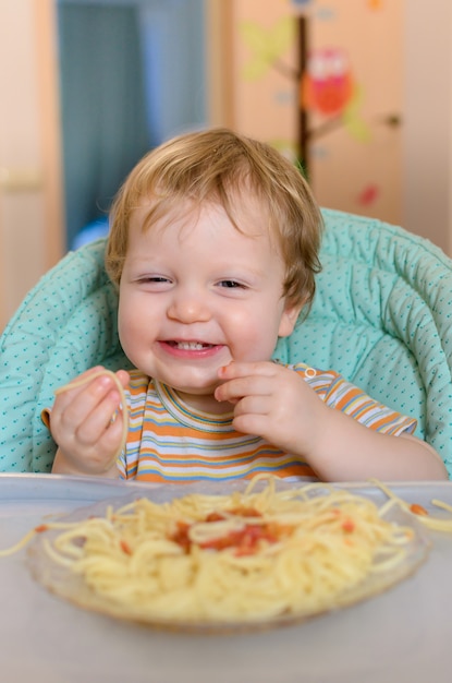 Süßes einjähriges Baby isst Spaghetti in einem Kinderstuhl.