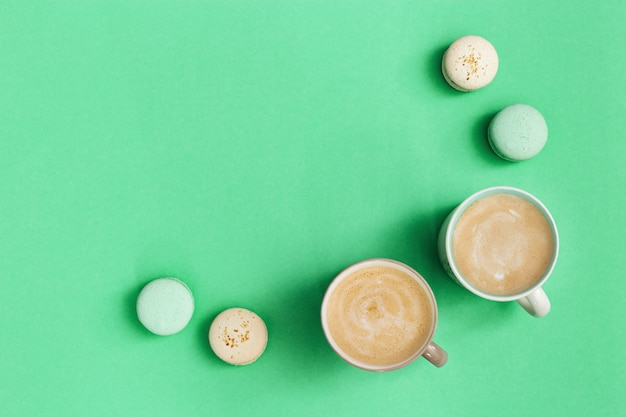 Süßes Essen, leckere Makronen und heißer duftender Kaffee mit Milchschaum. Zwei Tasse Cappuccino und köstliches Dessert auf Trendfarbe Minzhintergrund.