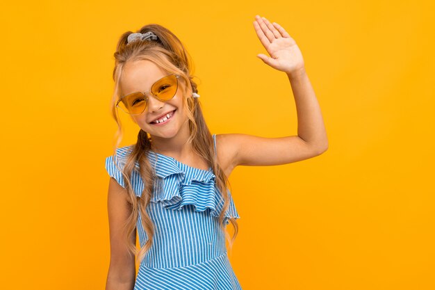 süßes europäisches Mädchen in der hellen Sonnenbrille zeigt eine Handfläche auf einer gelben Wand