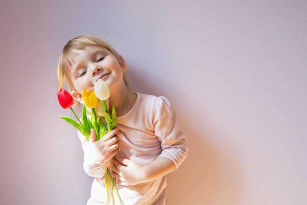 Süßes glückliches kleines blondhaariges Mädchen, das einen Strauß bunter Tulpen in ihren Händen hält