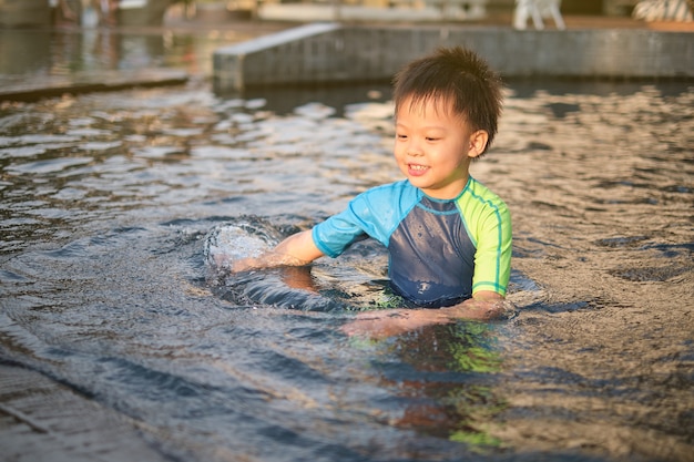 Süßes, glückliches, lächelndes kleines asiatisches 5-jähriges Jungenkind im Badeanzug, das an sonnigen Sommertagen im Schwimmbad spielt