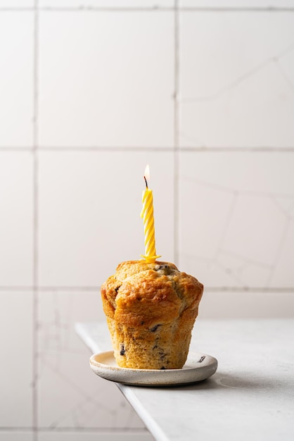 Süßes hausgemachtes Gebäck Muffin mit Blaubeeren und Kerze auf weißem Hintergrund minimalistisches Foto bi