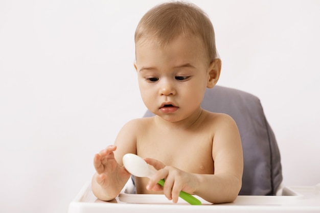 Süßes hungriges Baby, das mit einem Löffel im Hochstuhl sitzt