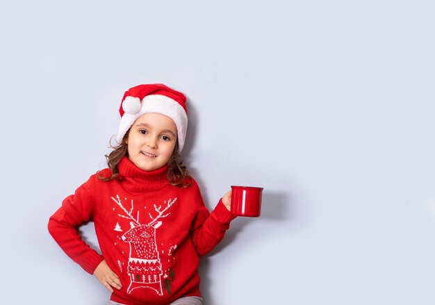 Süßes kaukasisches Kindermädchen in roter Weihnachtsmütze mit rotem Becher oder Tasse leerer Kopierraum für Design oder Text Banner Weihnachtsmockup-Vorlage