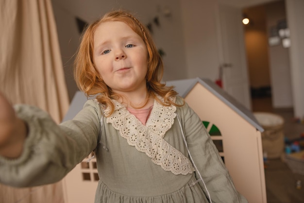 Süßes kaukasisches kleines Mädchen mit roten Haaren im Kleid blickt mit geschürzten Lippen auf die Kamera Baby Girl Concept