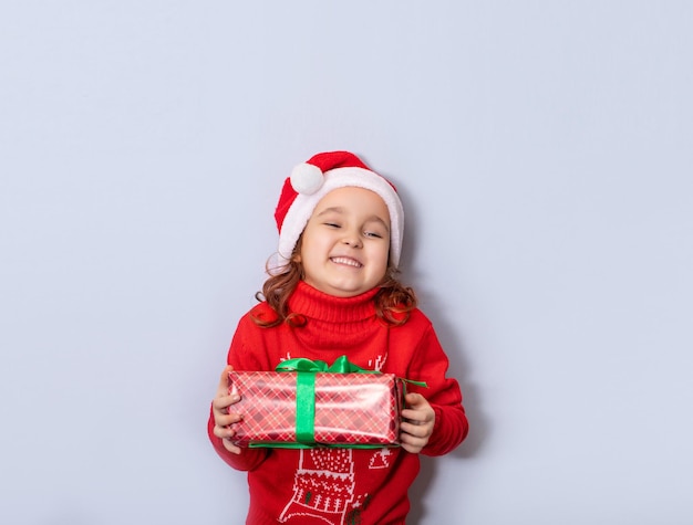 Süßes kaukasisches Mädchen in roter Weihnachtsmütze hält Geschenkbox und genießt Kopierplatz für Design oder Text Banner Weihnachtsmockup-Vorlage