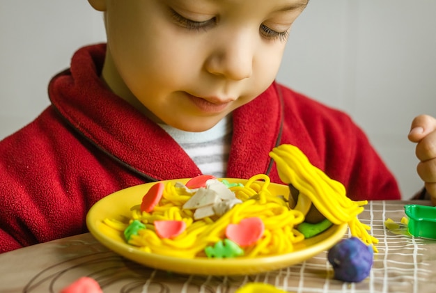 Süßes Kind, das sein originelles Spaghetti-Gericht aus buntem Plastilin sieht