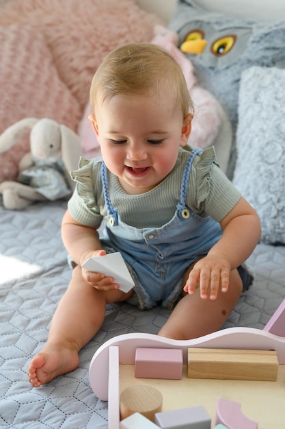 Süßes kleines Baby in lässiger Kleidung sitzt auf dem Bett und spielt zu Hause mit Spielzeugklötzen