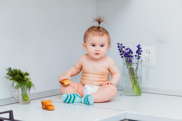 Süßes kleines Baby mit Keksen, das auf dem Tisch in der Küche sitzt