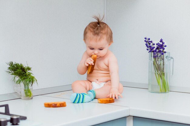 Süßes kleines Baby mit Keksen, das auf dem Tisch in der Küche sitzt