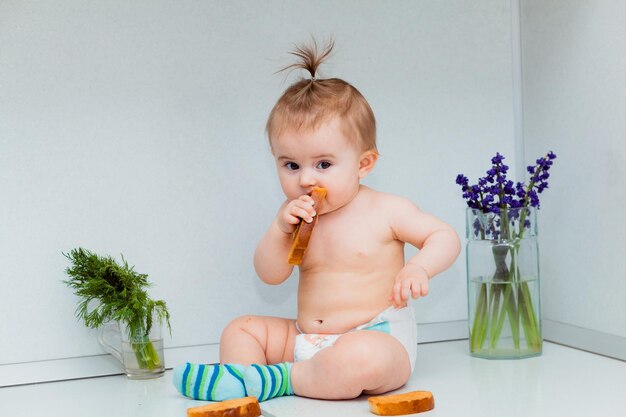 Süßes kleines Baby mit Keksen, das auf dem Tisch in der Küche sitzt