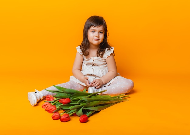 Süßes kleines blondes Mädchen mit einem Strauß Tulpen in einem Baumwollkleid auf rosa Hintergrund 8. März