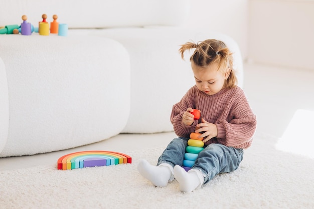 Süßes kleines Kleinkind, das zu Hause mit Öko-Holzspielzeug spielt Glückliches Kind, das Gemüse und Obst mit Spielzeugmesser schneidet Das Kind spielt Lernspiele