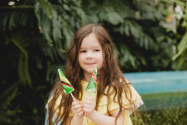 Süßes kleines Mädchen, das einen wassermelonenförmigen Lutscher isst Kind mit Lutschern im botanischen Garten