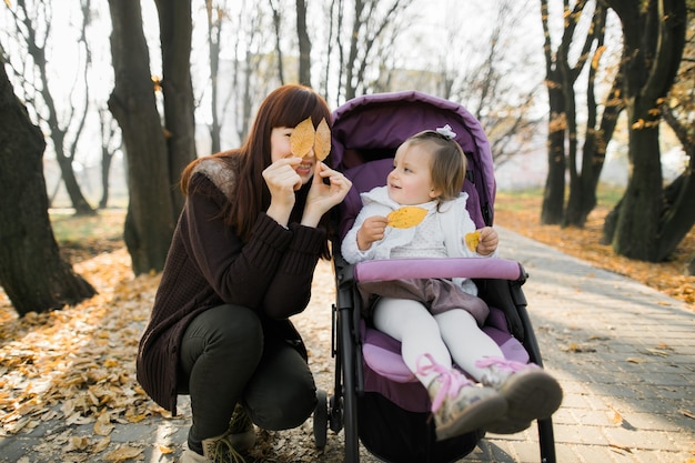 süßes kleines Mädchen, das im lila Kinderwagen neben ihrer Mutter sitzt