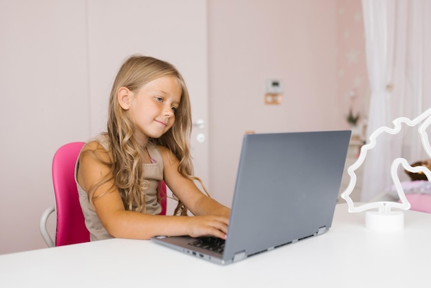 Süßes kleines Mädchen, das zu Hause auf einem Laptop spielt Heimunterricht und Bildung Online-Lernen Fernunterricht Hausaufgaben Lifestyle-Konzept von Schulmädchen