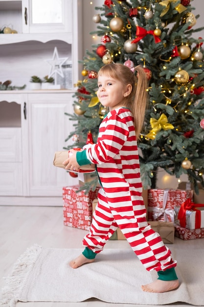 süßes kleines Mädchen im Weihnachtspyjama mit Geschenkboxen unter dem Weihnachtsbaum zu Hause