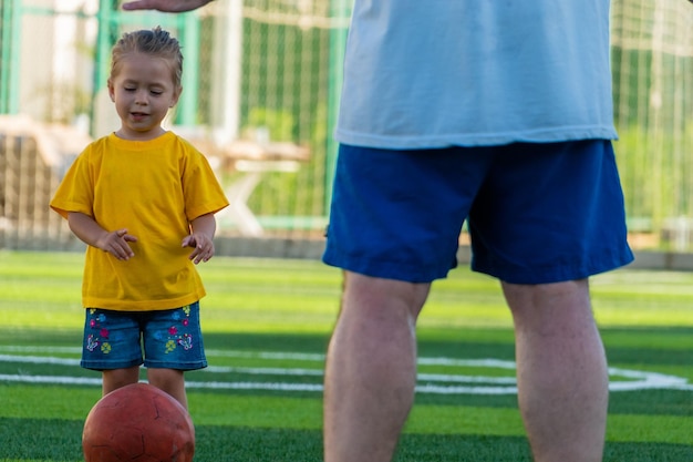 Foto süßes kleines mädchen in gelbem t-shirt wird den ball an vater treten