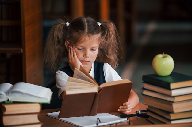 Süßes kleines Mädchen mit Zöpfen ist in der Bibliothek