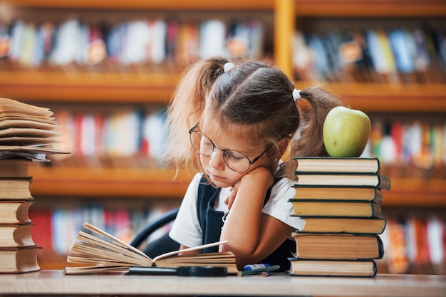 Süßes kleines Mädchen mit Zöpfen ist in der Bibliothek