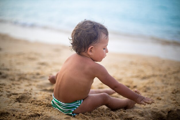 süßes Kleinkind, das im Sand am Meer spielt.