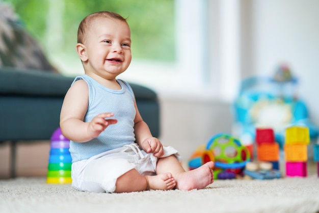 süßes lächelndes Baby, das im Wohnzimmer auf dem Boden sitzt und spielt