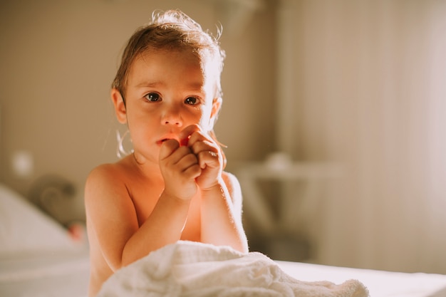 Süßes lockiges kleines Mädchen mit einem Tuch über ihrem nassen Körper, der in einem Schlafzimmer nach Dusche stationiert