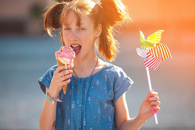 Süßes Mädchen, das Eis auf sommerlichem Hintergrund im Freien isst Nahaufnahmeporträt eines entzückenden rothaarigen kleinen Mädchens, das Eis isst