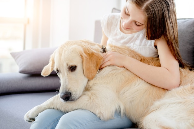 Süßes Mädchen, das niedlichen Hund hält, der auf Sofa drinnen sitzt