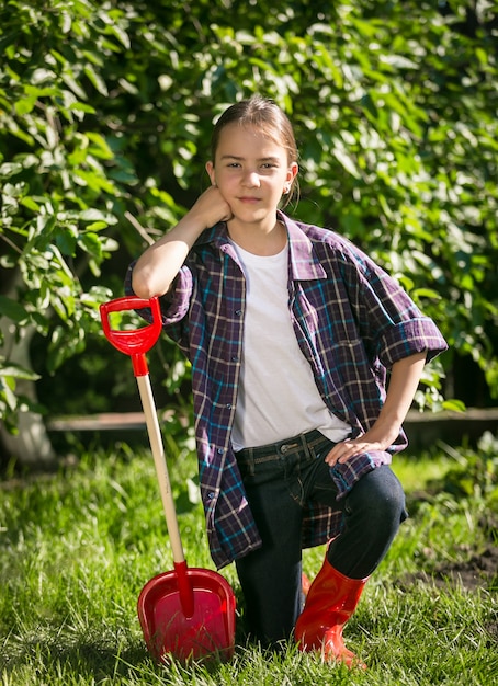 Süßes Mädchen in Gummistiefeln posiert mit Spielzeugspaten im Garten