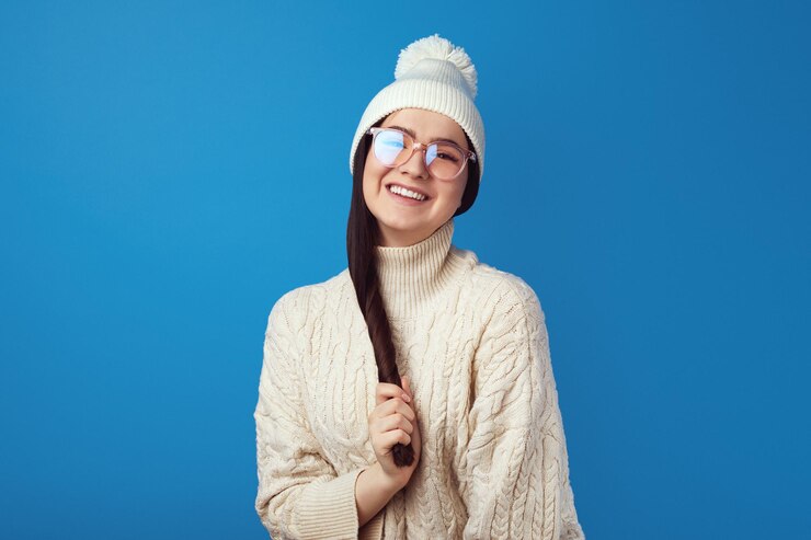 Süßes Mädchen lächelt in die Kamera, trägt weißen Hut und gestrickte weiße Übergröße
