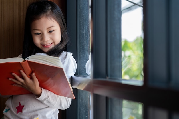 süßes Mädchen lächelte und stand zum Lesen Buch in der Bibliothek