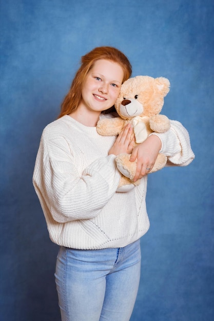 Süßes Mädchen mit roten Haaren in einem weißen Pullover und Jeans umarmt ein Plus