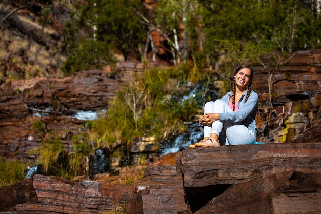 Süßes Mädchen mit Zöpfen sitzt auf geschichteten roten Steinen im Karijini-Nationalpark in Westaustralien