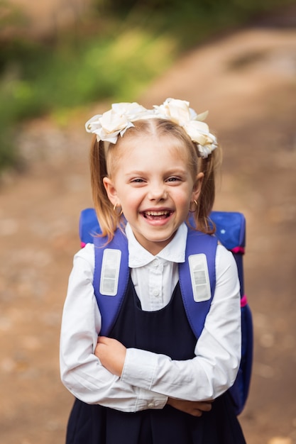 Foto süßes mädchen, schüler in schuluniform mit rucksack, lächelnd